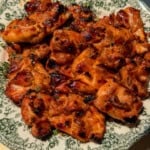 A plate of grilled chicken pieces, charred and glazed, served on a decorative green and white floral-patterned dish under bright lighting—perfect to enjoy before indulging in a refreshing Viral Melon Ice Cream (2 Ingredients) for dessert.