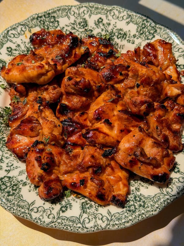 A plate of grilled chicken pieces, charred and glazed, served on a decorative green and white floral-patterned dish under bright lighting—perfect to enjoy before indulging in a refreshing Viral Melon Ice Cream (2 Ingredients) for dessert.
