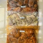 Three labeled ziplock bags filled with flavorful chicken marinades: one with garlic and honey, one with Greek lemon, and one with peri peri. Each marinade is seasoned with herbs and spices, and the bags are arranged vertically.