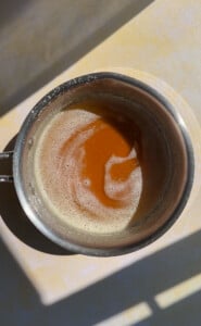 A stainless steel pot with browned butter inside, showing a caramel-colored swirl, sits on a sunlit countertop with shadows crossing over it—perfect for elevating your favorite chicken marinades.