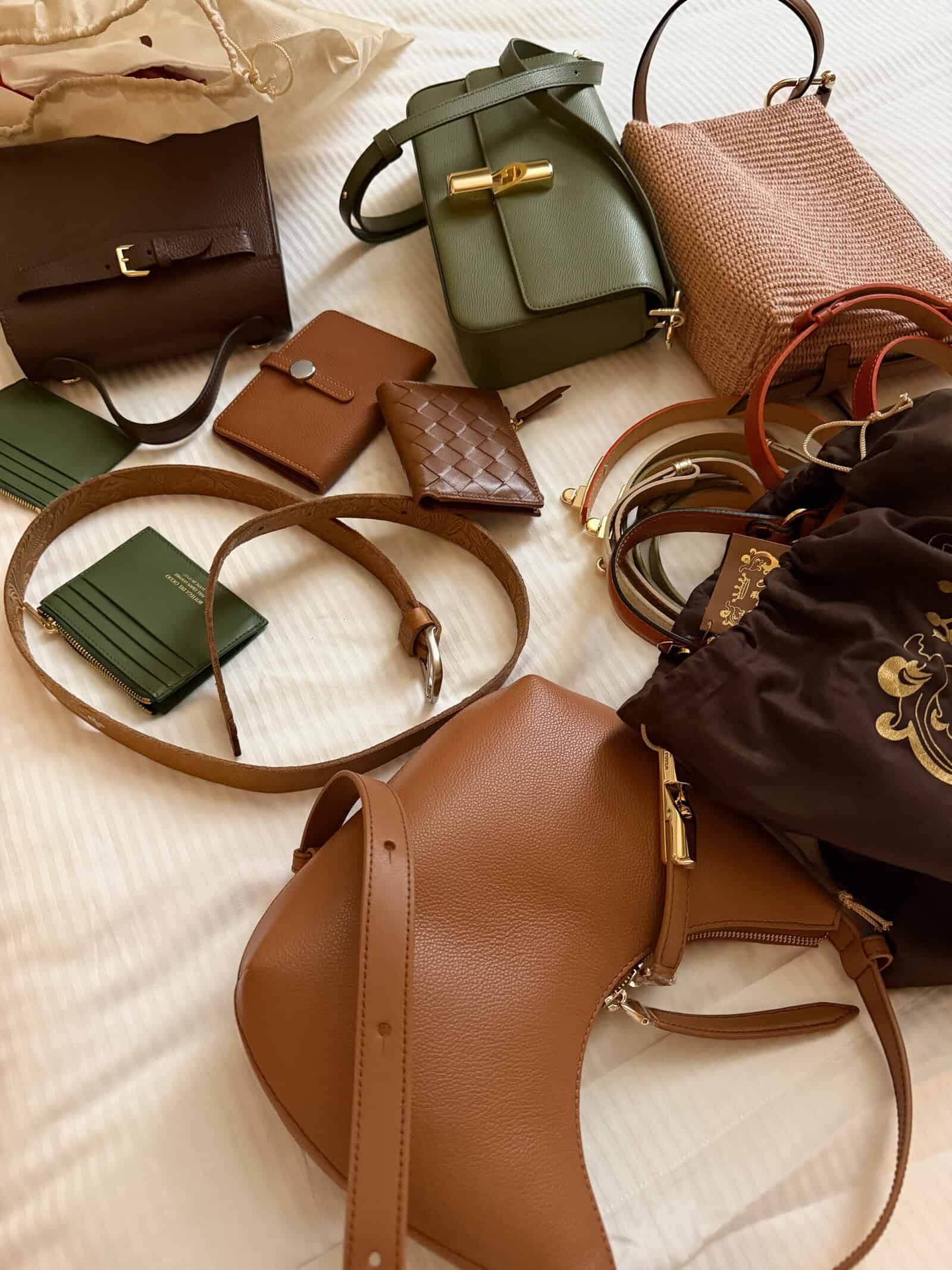 Various handbags, wallets, belts, and pouches in brown, green, and pink tones are spread out on a white surface.