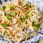 A bowl of creamy spaghetti topped with toasted pine nuts and fresh mint leaves, served in a blue and white patterned dish with a fork resting inside.