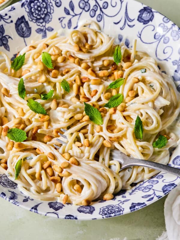 A bowl of creamy spaghetti topped with toasted pine nuts and fresh mint leaves, served in a blue and white patterned dish with a fork resting inside.