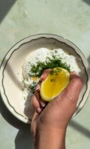 Hand squeezing lemon over creamy dill sauce in bowl