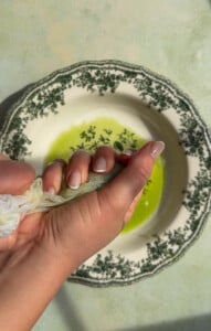 Hands squeezing green juice through cheesecloth over decorative plate