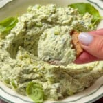 Hand dipping a chip into creamy green herb dip