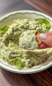 Hand dipping a chip into creamy green herb dip
