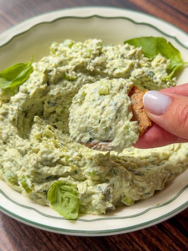 Hand dipping a chip into creamy green herb dip