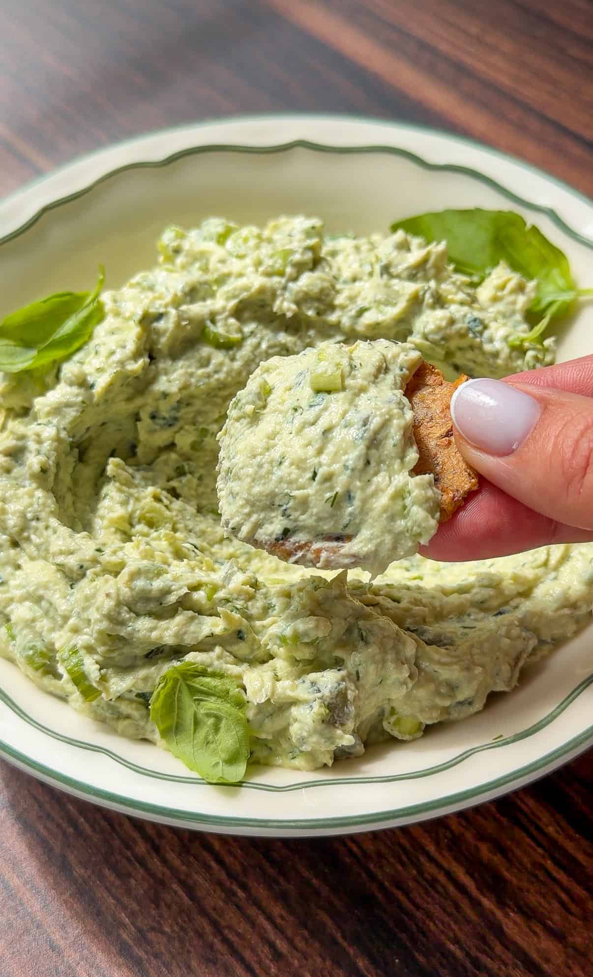 Hand dipping a chip into creamy green herb dip