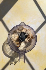 Cooked chicken pieces inside a KitchenAid food processor bowl