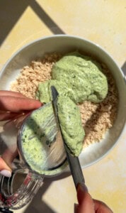 Green herb sauce being added to breadcrumbs in bowl