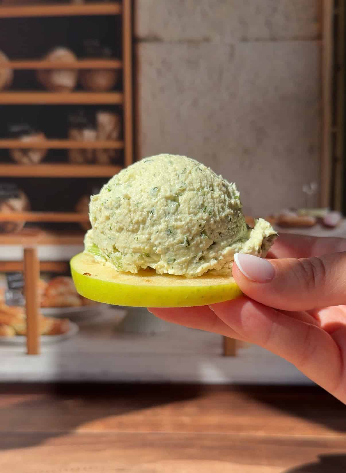 Hand holding herb cheese scoop on fresh apple slice