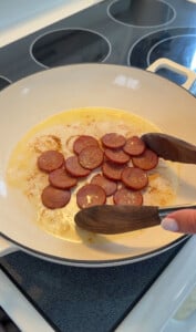 Sliced sausage cooking in white skillet on stovetop