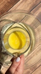 Hand holding measuring cup with melted butter over bowl