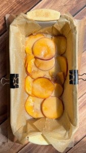 Sliced peaches layered in parchment-lined loaf pan
