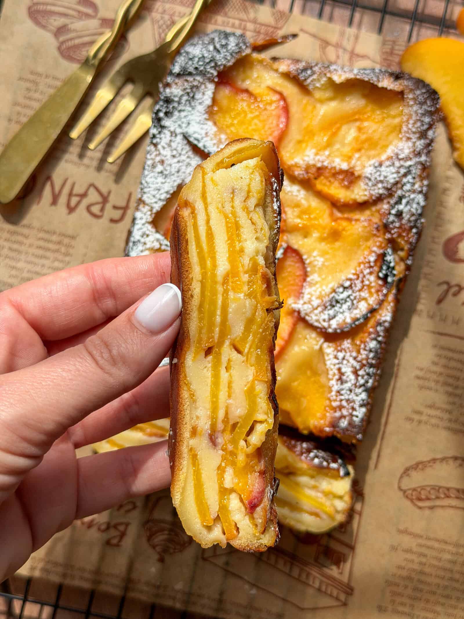 Hand holding a slice of peach cake dusted with powdered sugar