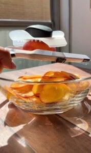 Mandoline slicer cutting fresh peaches into glass bowl