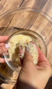 Hands rubbing lemon zest into sugar in glass bowl