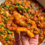 Hand holding fried bread dipped in butter chicken beans