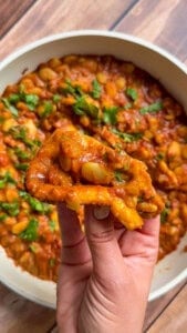 Hand holding fried bread dipped in butter chicken beans