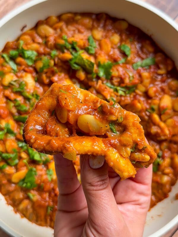 Hand holding fried bread dipped in butter chicken beans