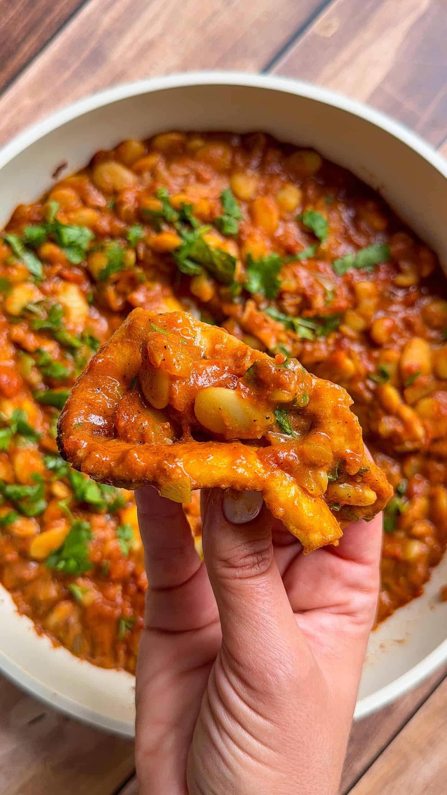 Hand holding fried bread dipped in butter chicken beans