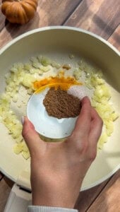 Hand adding spices to sautéed onions in a pot