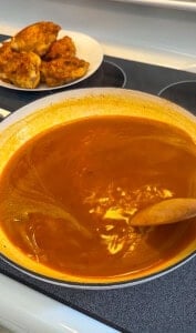 Rich tomato sauce simmering in pan with seasoned chicken pieces