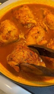 Chicken thighs simmering in rich orange curry sauce