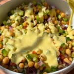 Creamy dressing being poured over chickpea salad bowl