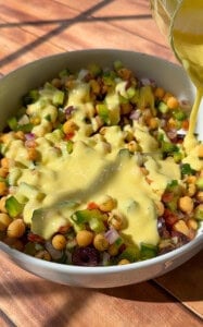 Creamy dressing being poured over chickpea salad bowl