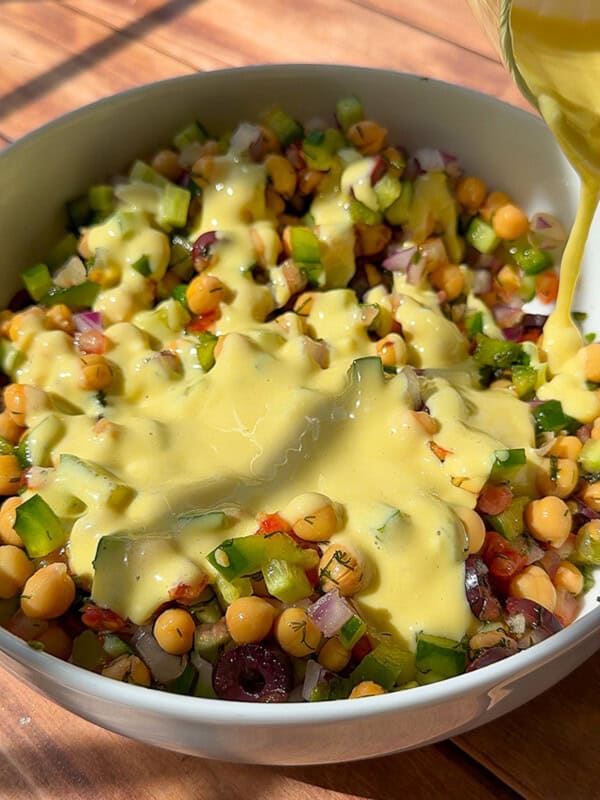 Creamy dressing being poured over chickpea salad bowl