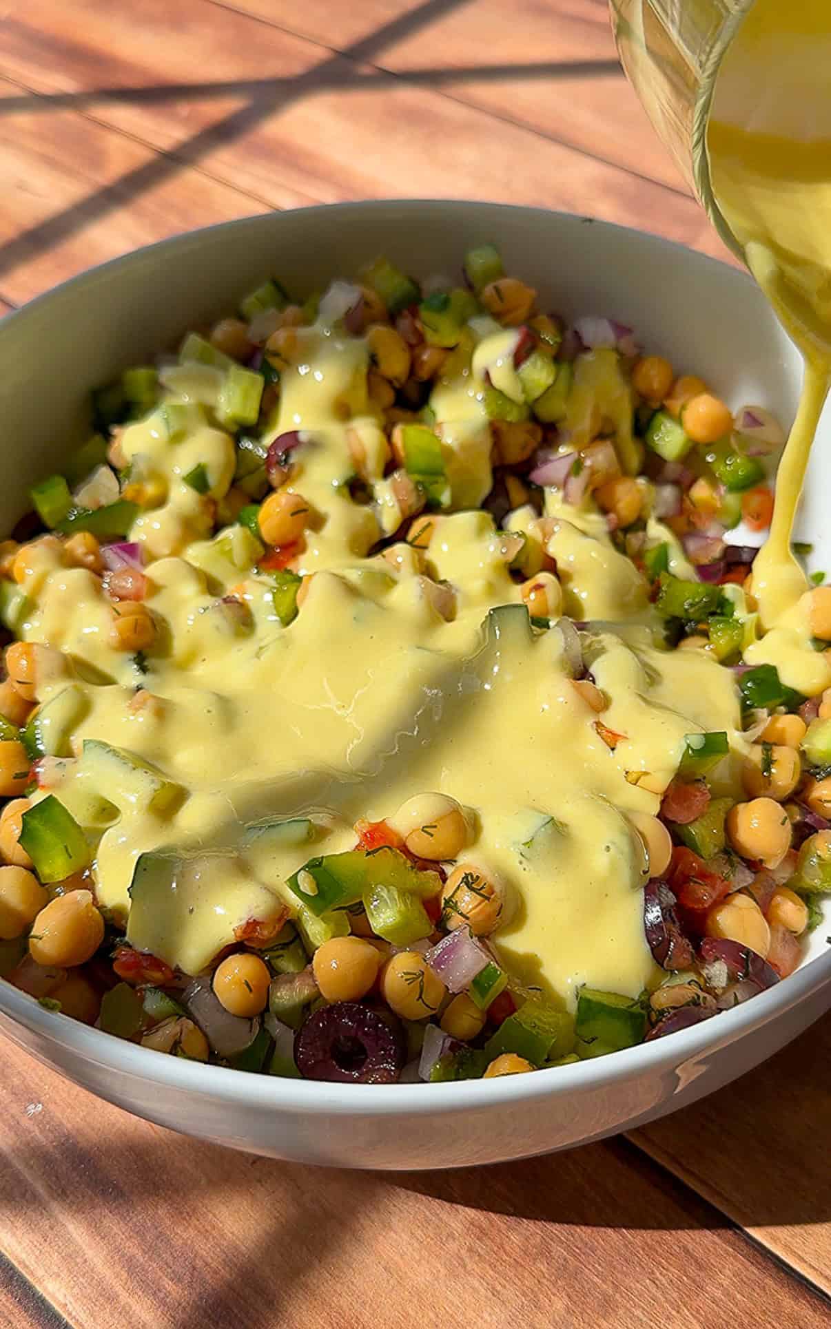 Creamy dressing being poured over chickpea salad bowl