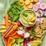Colorful vegetable and cracker platter with green hummus dip