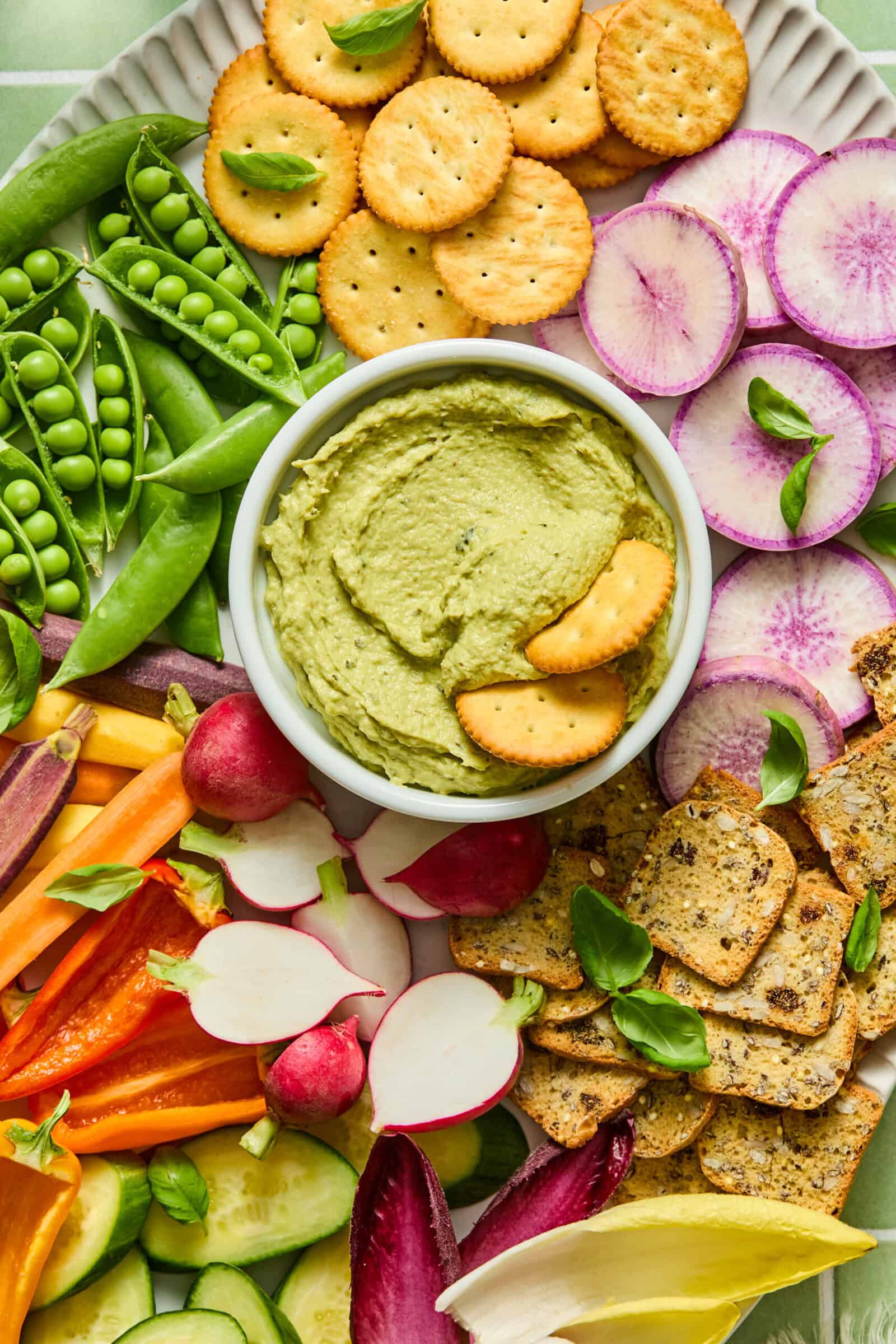 Colorful vegetable platter with green hummus dip and crackers