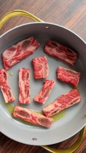 Raw beef short ribs searing in a gray nonstick pan