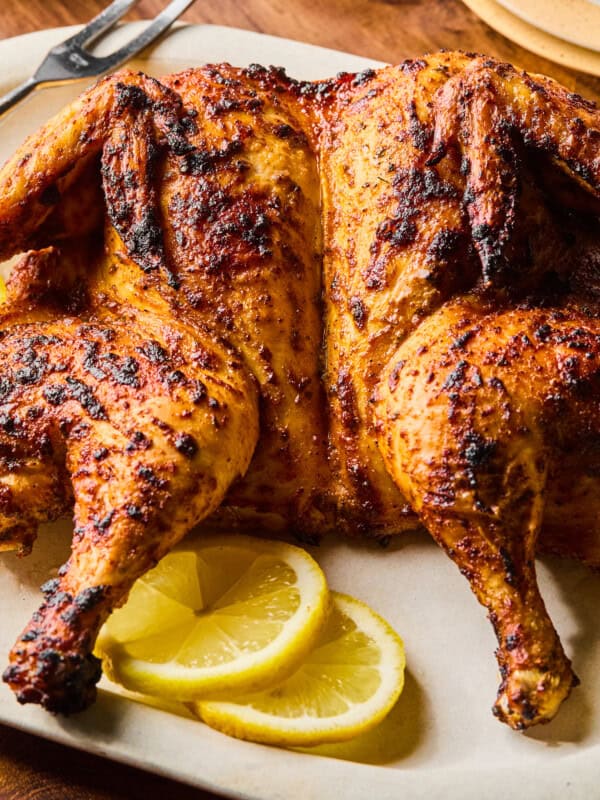 Golden spatchcock roasted chicken with lemon slices on platter